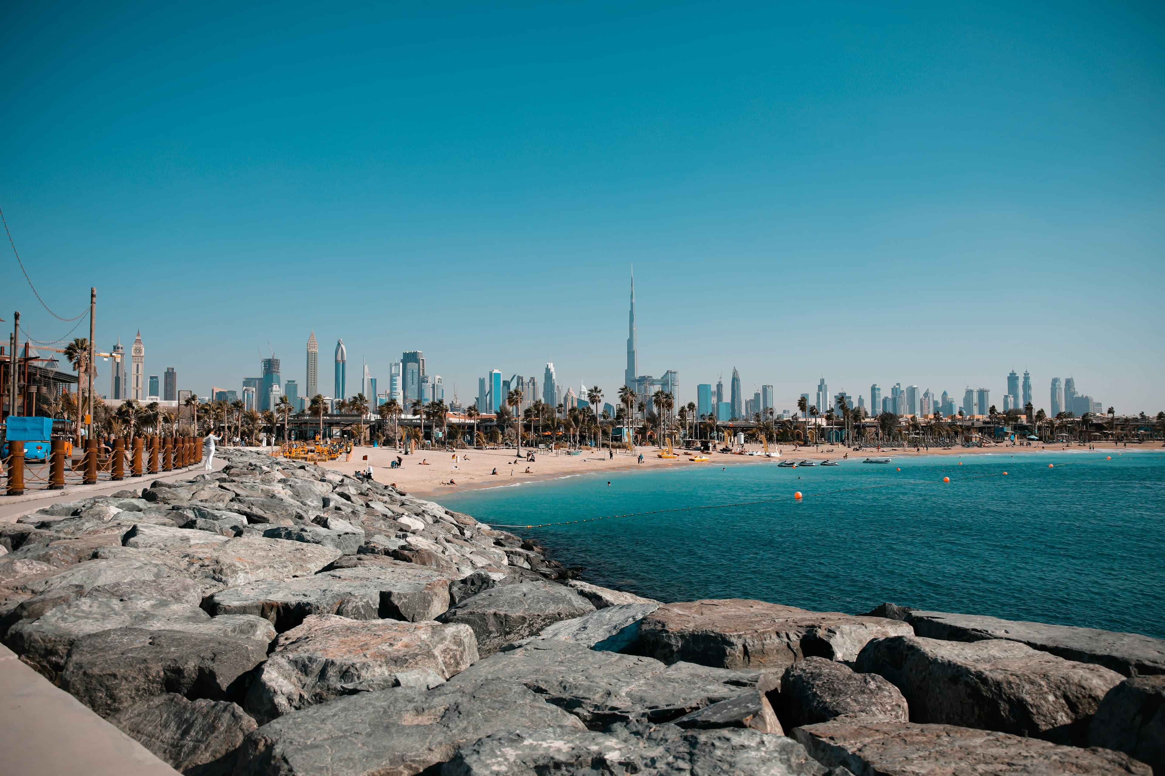 The beach at La Mer on a clear day, with palm trees along the sand and the Burj Khalifa and Downtown Dubai skyline behind