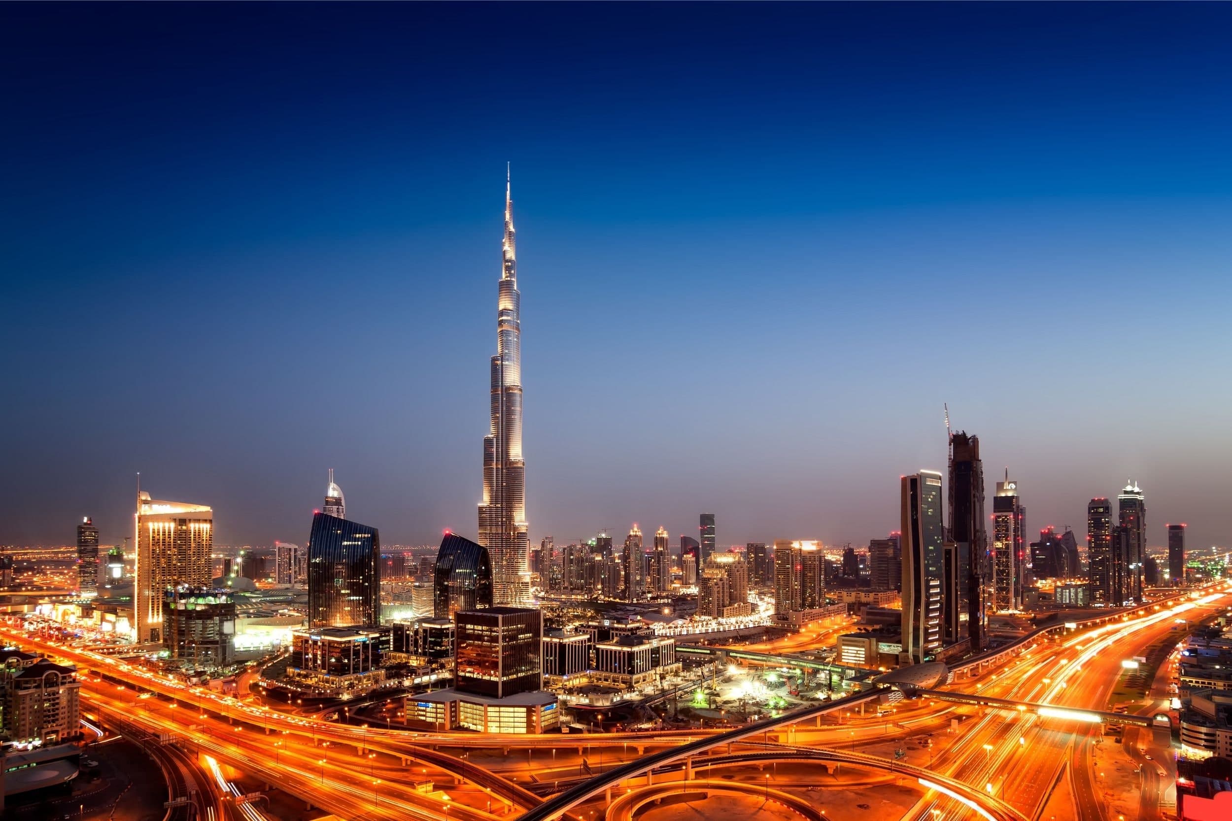 The Burj Khalifa above the Downtown Dubai skyline at dusk, with traffic on the roads below