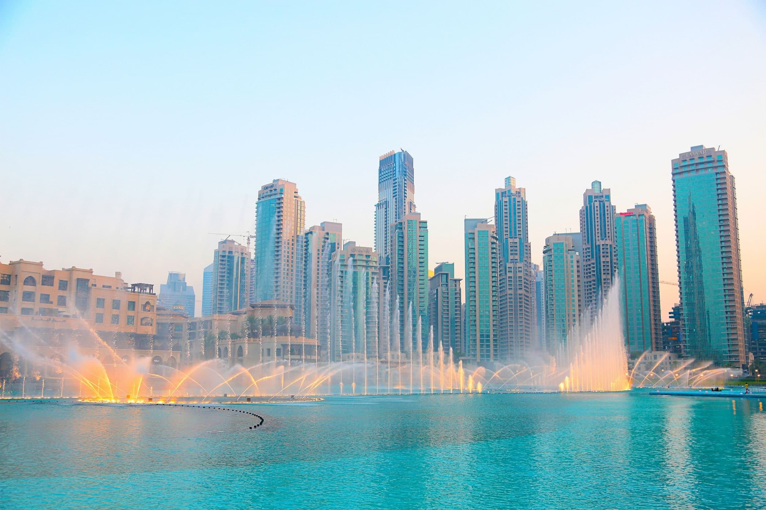The Dubai Fountain lit gold in the early evening, with the residential towers of Downtown Dubai behind it