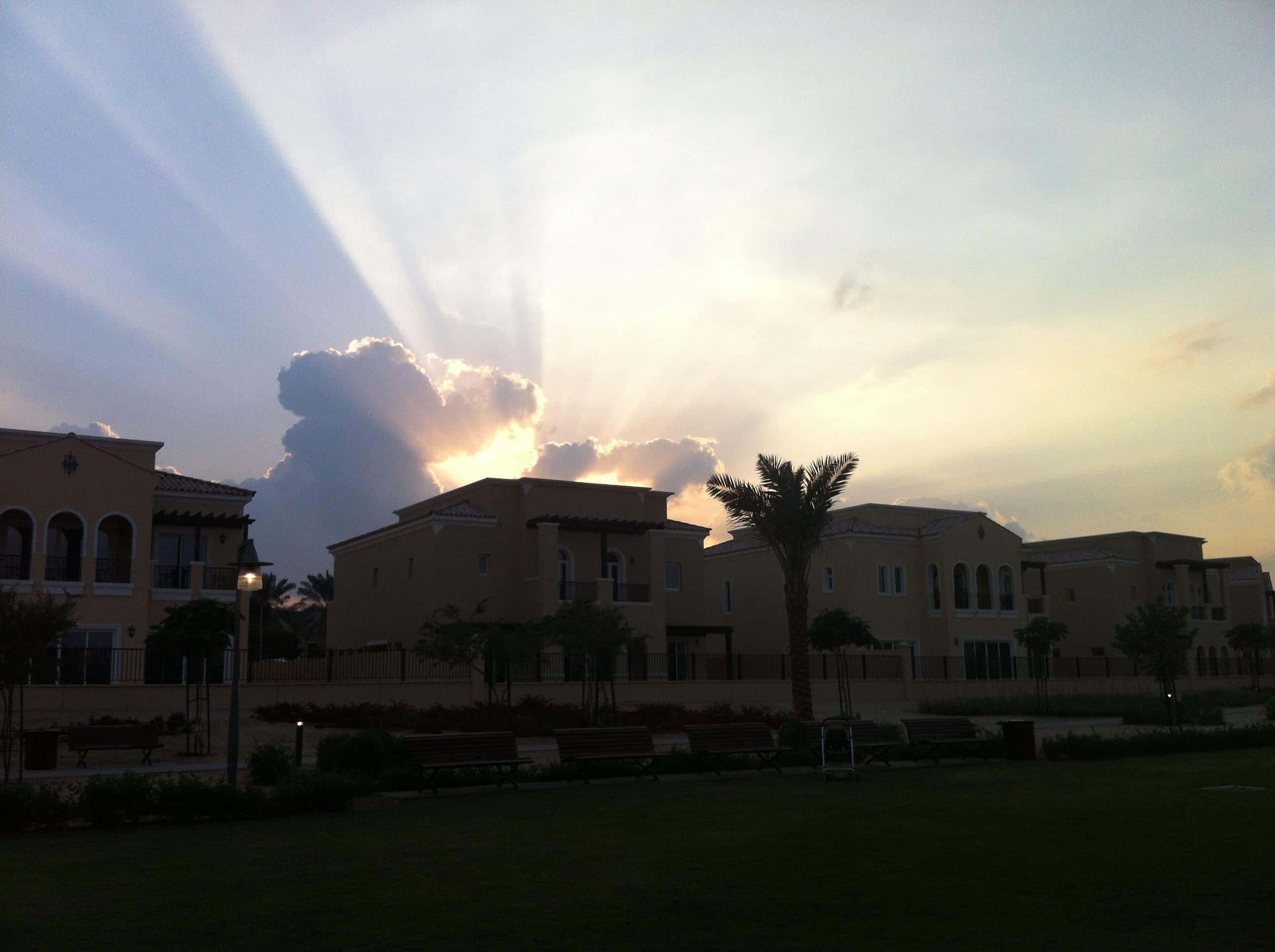 Two-storey villas with tiled roofs and arched windows facing a landscaped park in Arabian Ranches at sunset