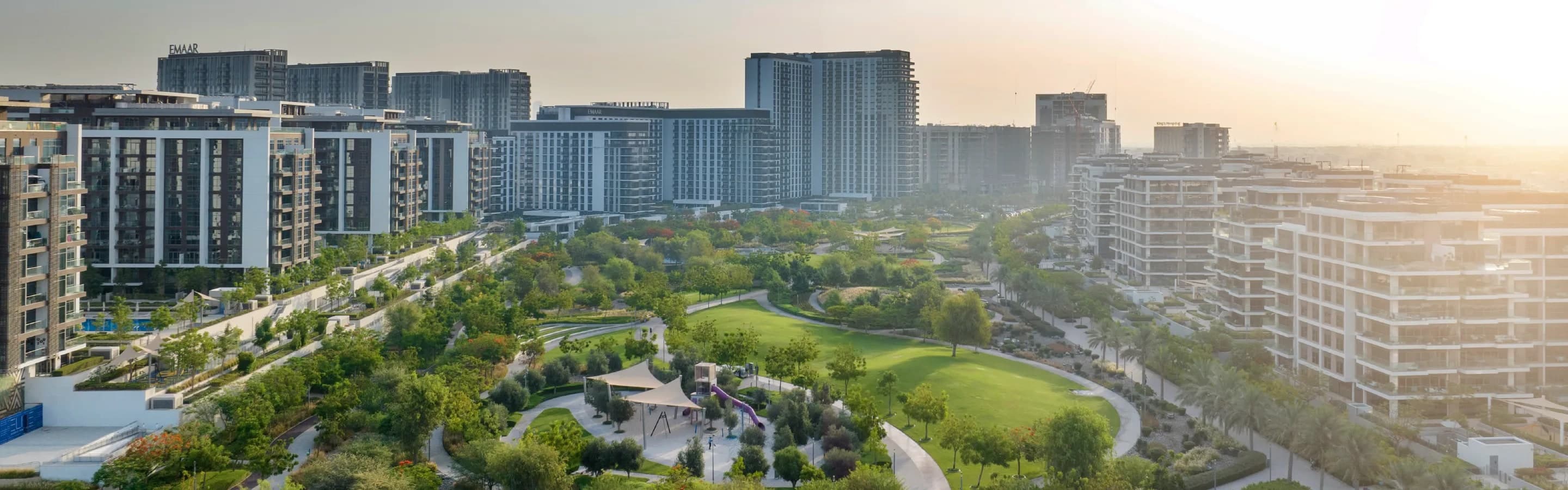 An aerial view of Dubai Hills Park, with its lawns, trees and play area surrounded by mid-rise apartment buildings