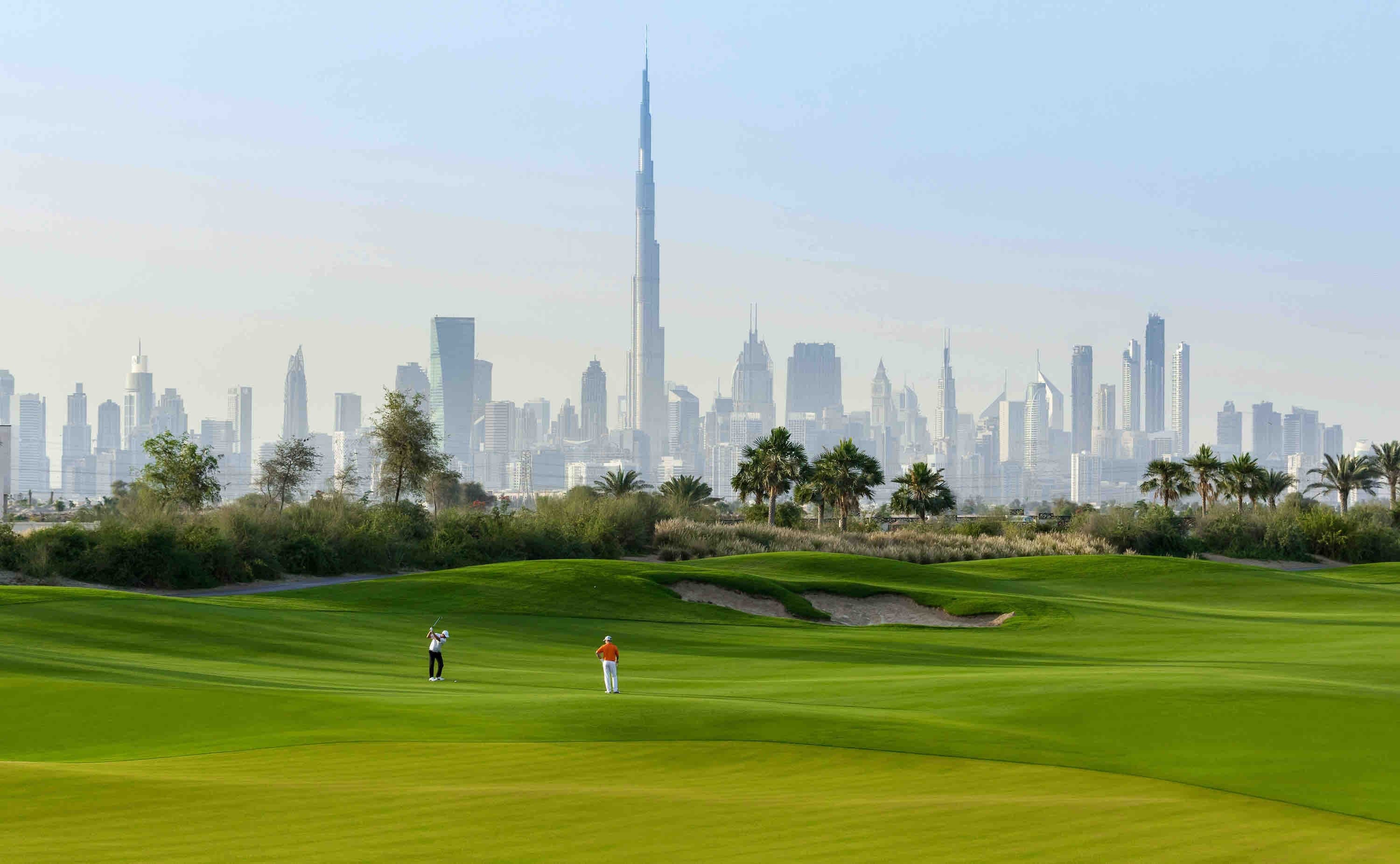 Golfers on a fairway of the Dubai Hills Golf Club, with the Burj Khalifa and the Downtown Dubai skyline in the distance