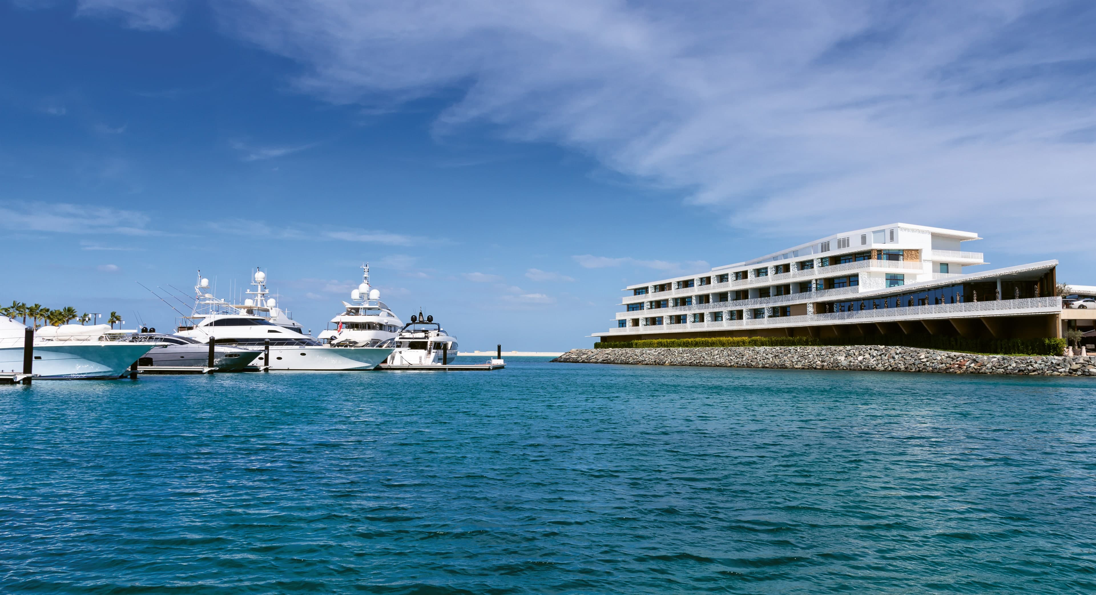 The white Bulgari Yacht Club building on Jumeirah Bay Island seen from the sea, with large yachts moored at the marina entrance