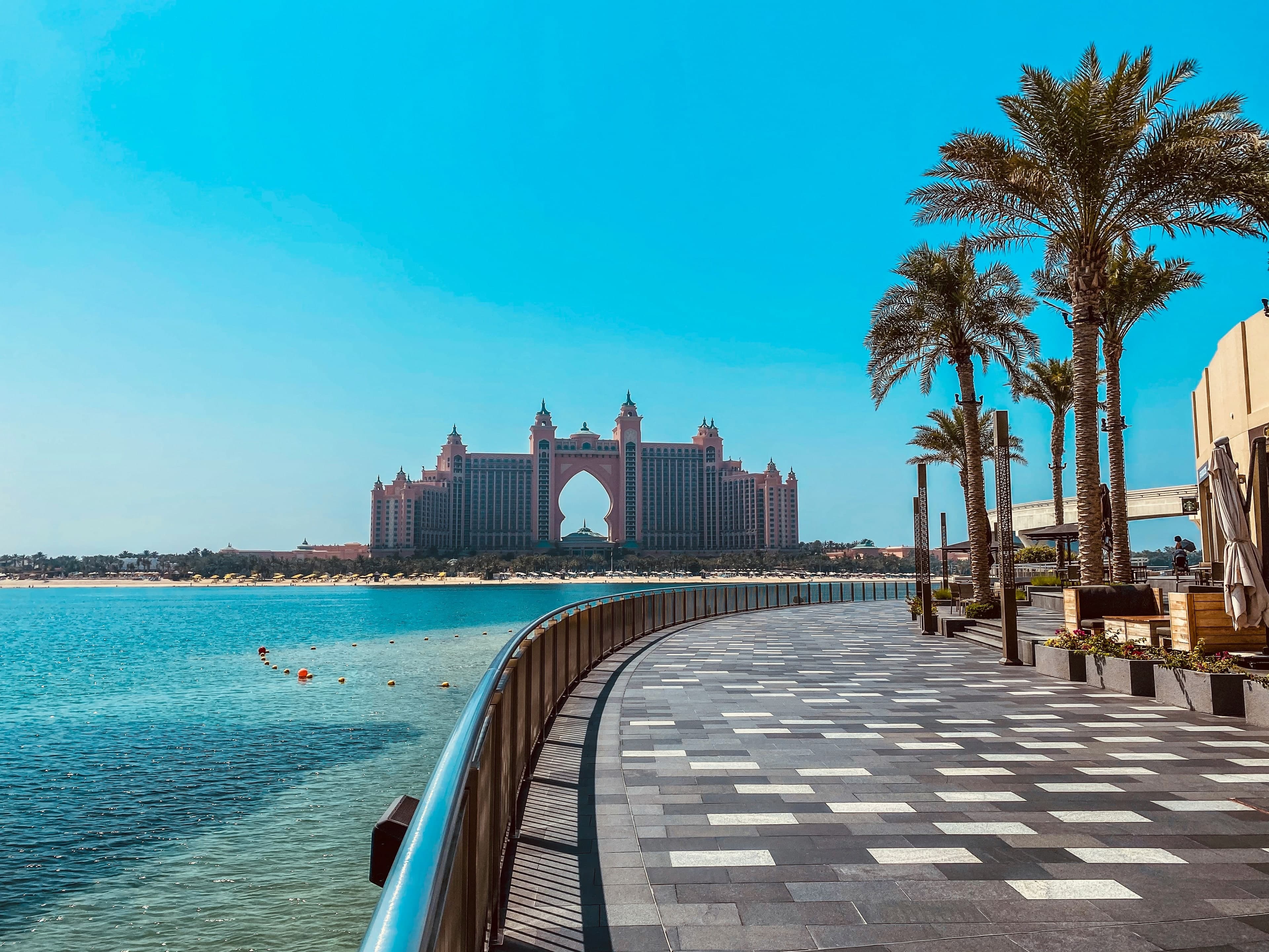 A curving waterfront walkway with palm trees on Palm Jumeirah, with Atlantis The Palm across the water