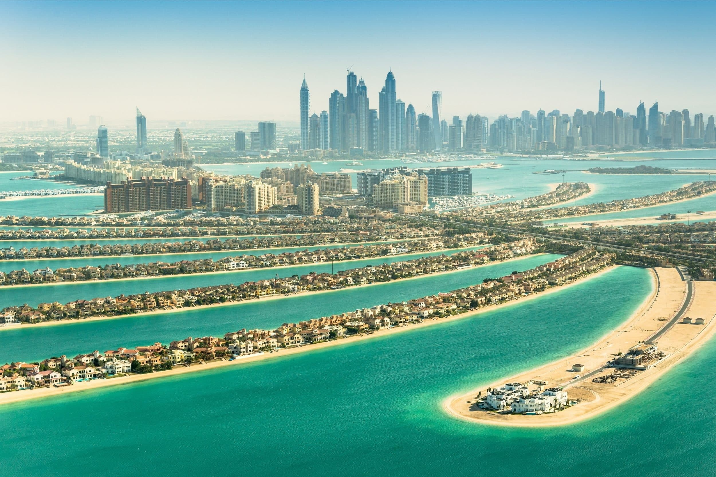 Villas lining the curved fronds of Palm Jumeirah, with turquoise water between them and the Dubai Marina towers on the horizon