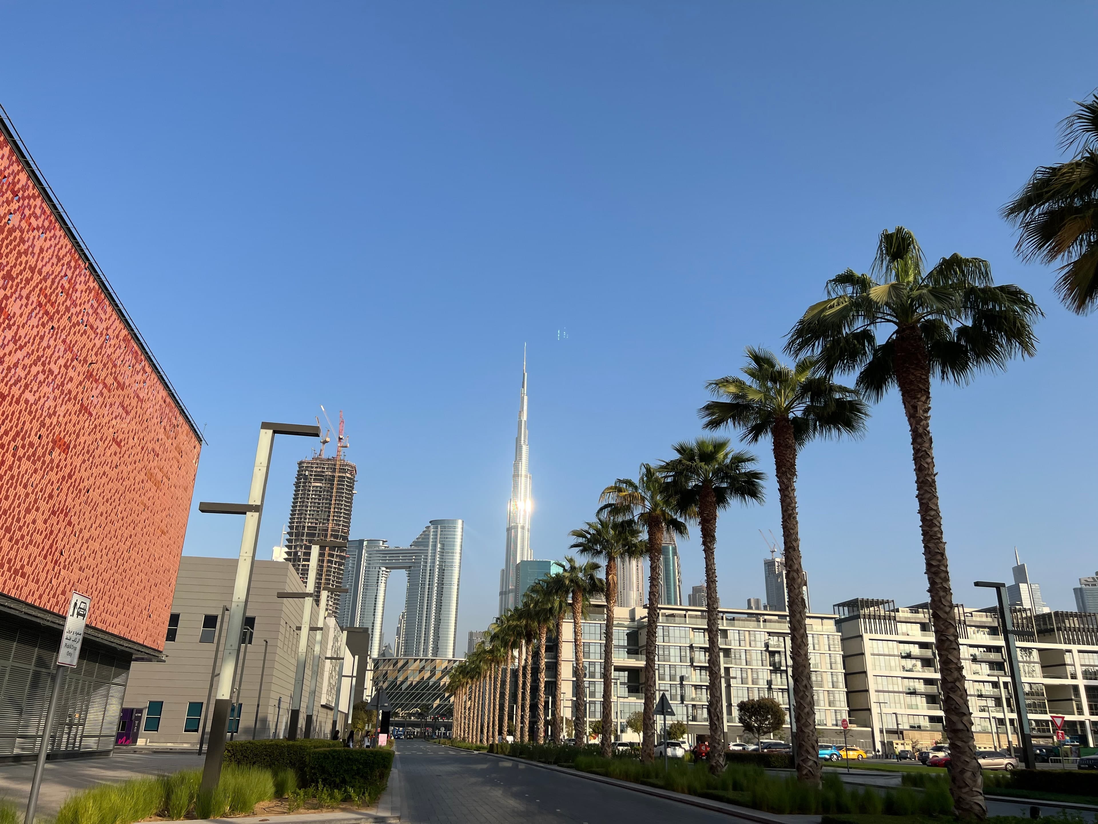 A palm-lined street in City Walk on a clear day, with low-rise apartment buildings on the right and the Burj Khalifa rising ahead