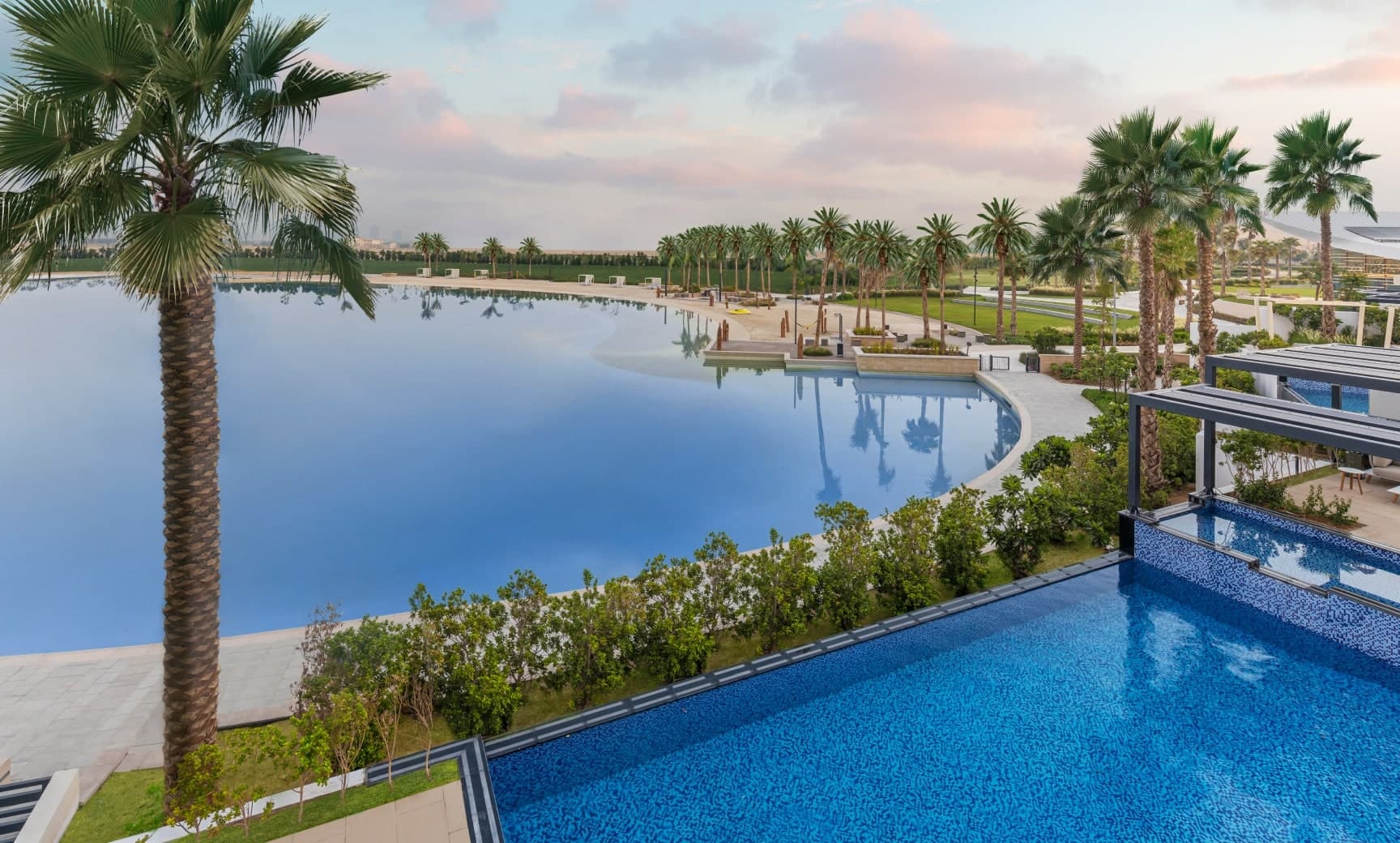 View across Lagoon Al Ghaf from a home's terrace pool, with palm trees and the lagoon beach curving around the far shore