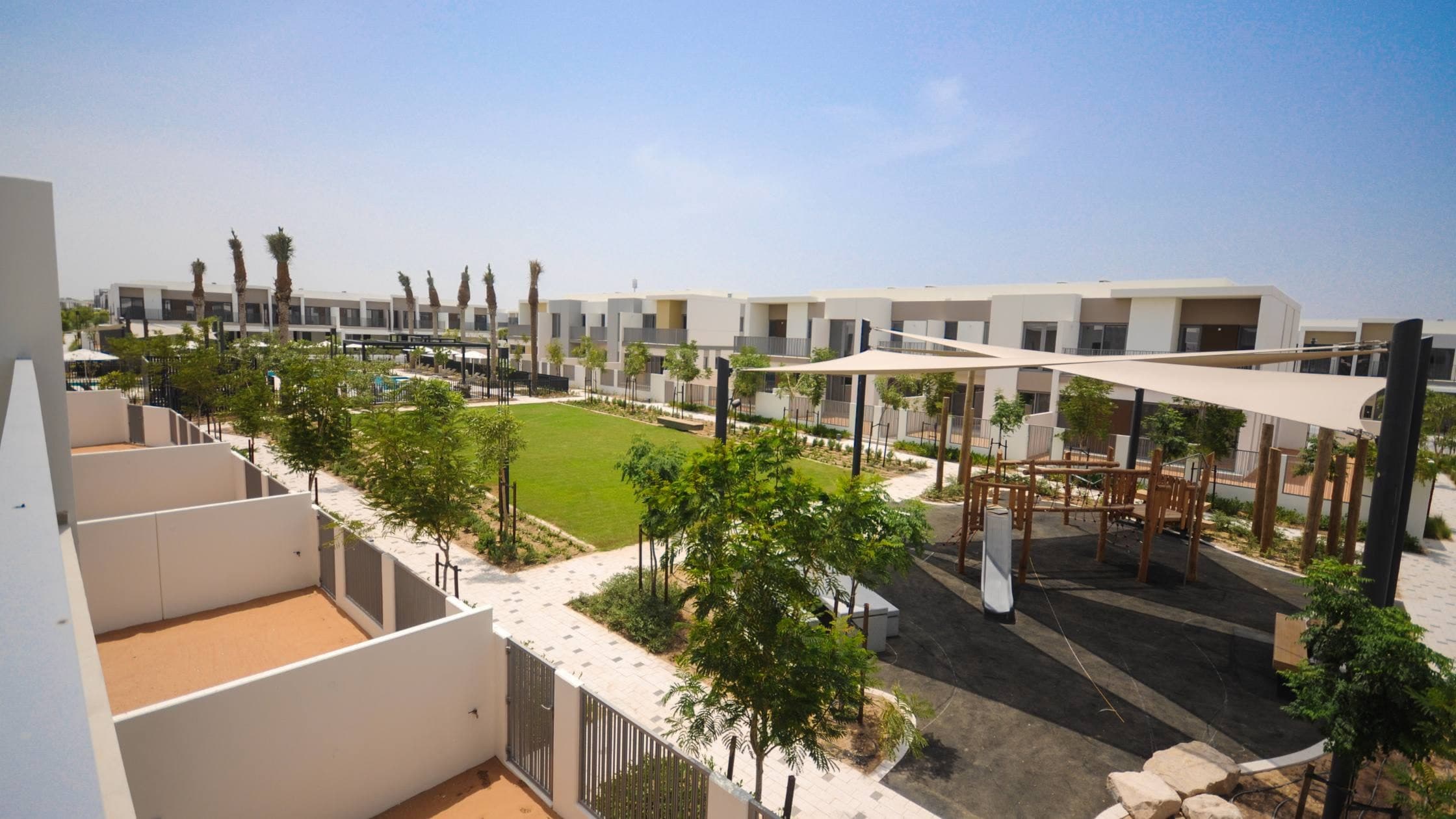 Rows of white townhouses in Tilal Al Ghaf around a shared lawn and a shaded children's play area