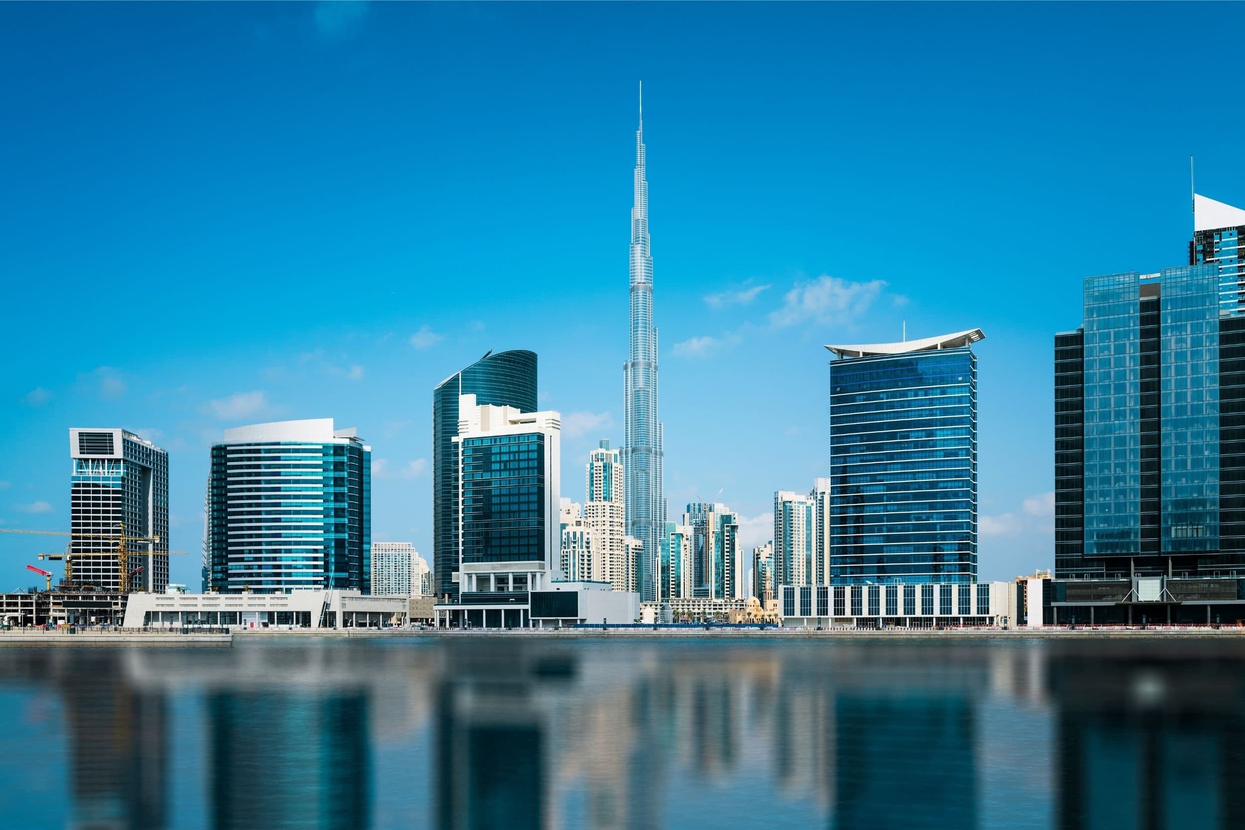 Glass office and residential towers along the Dubai Water Canal in Business Bay, with the Burj Khalifa rising behind them