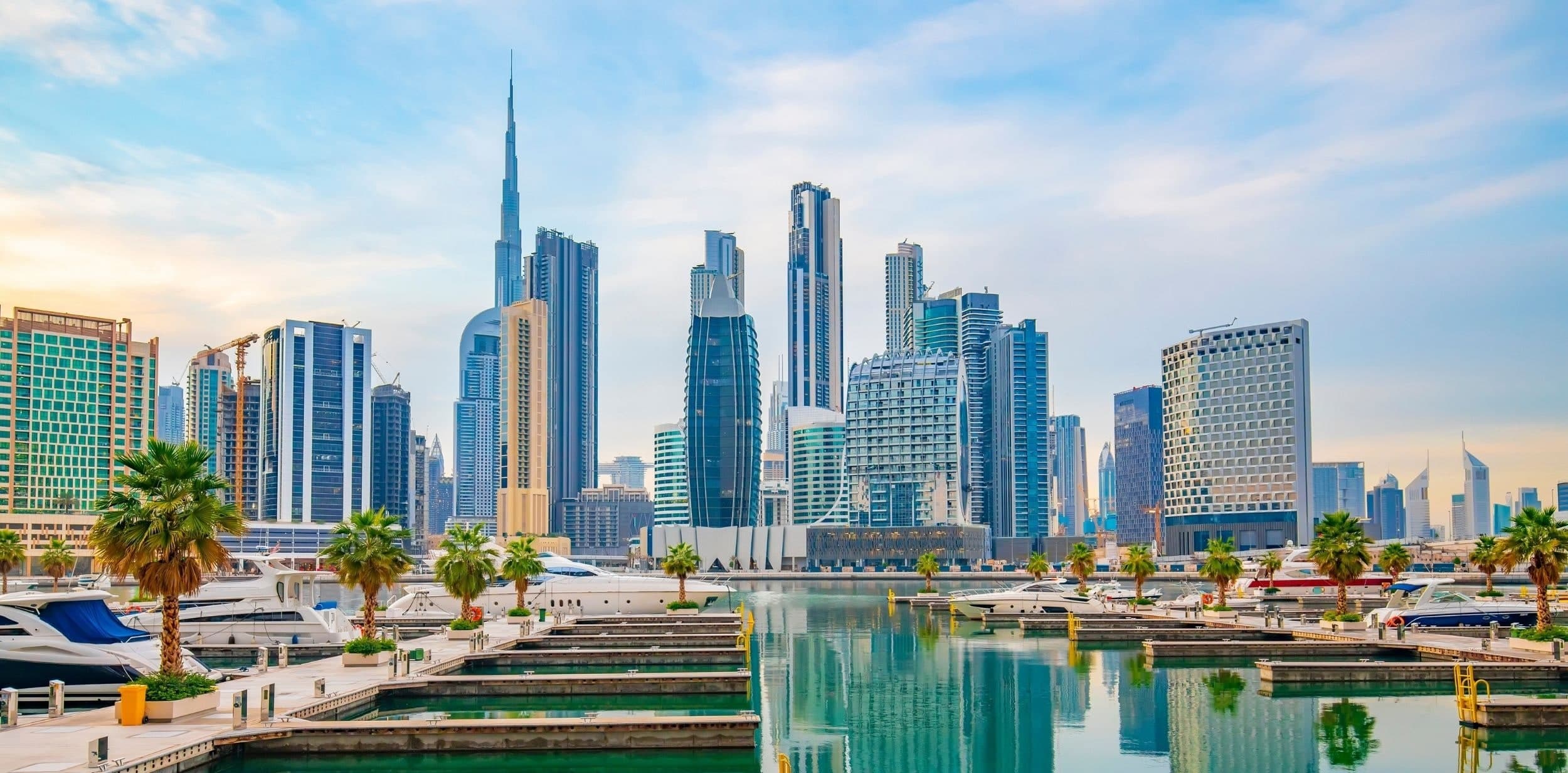 Yachts moored at a marina in Business Bay, with palm trees on the jetties and towers and the Burj Khalifa behind