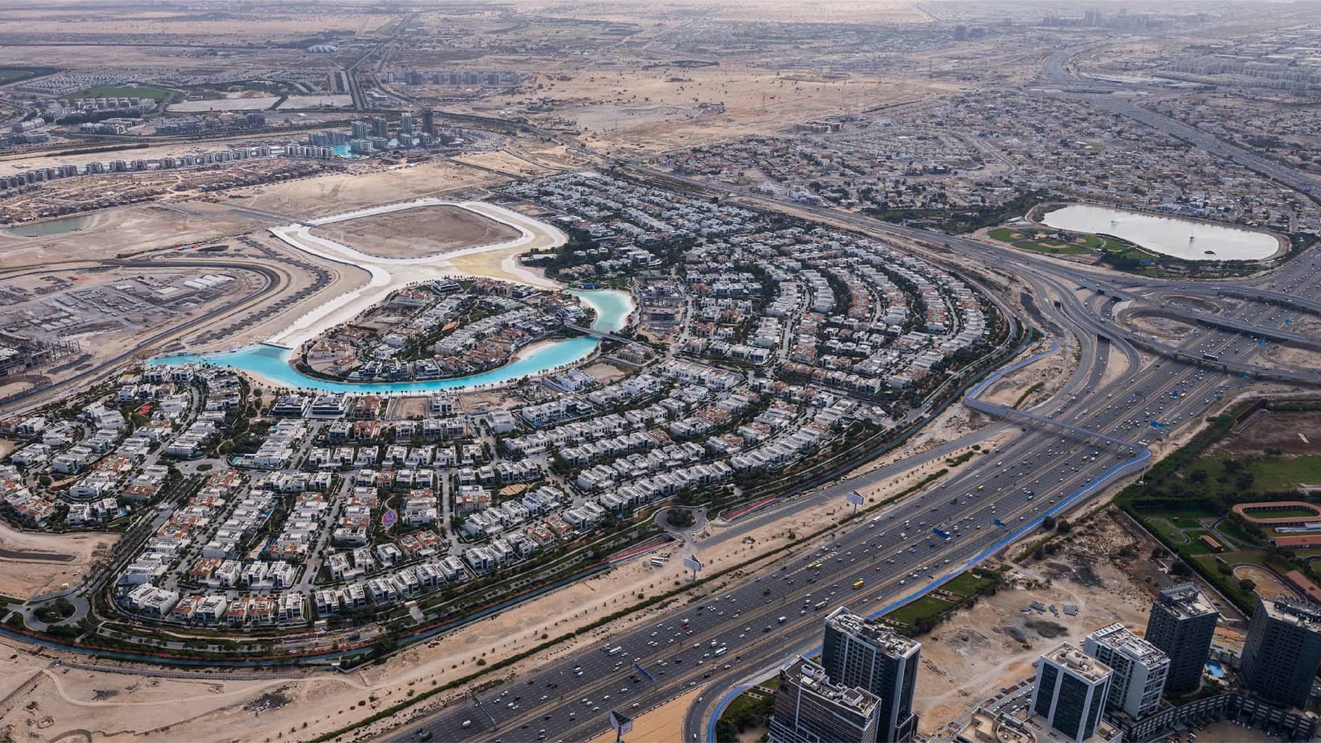 High aerial view of the District One villa community wrapped around a turquoise lagoon, with Al Khail Road running alongside
