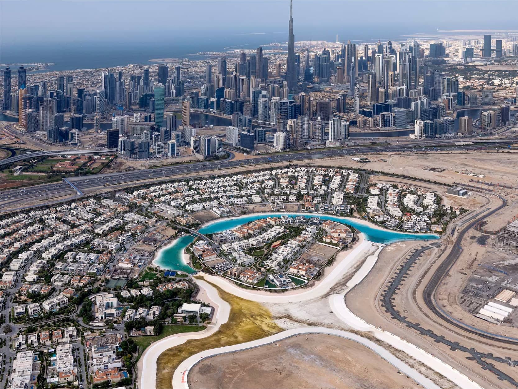 Aerial view of the Crystal Lagoon curving around an island of villas in District One, with Business Bay and Downtown Dubai beyond