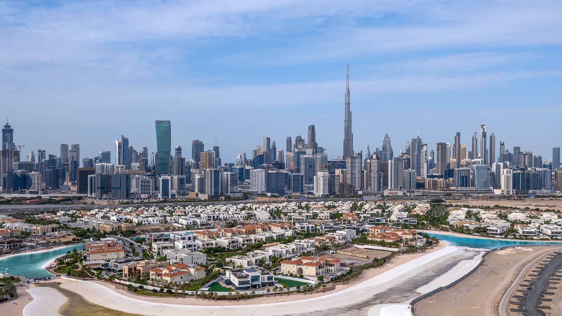 Villas with red and white roofs along the Crystal Lagoon in District One, with the Downtown Dubai skyline and the Burj Khalifa behind