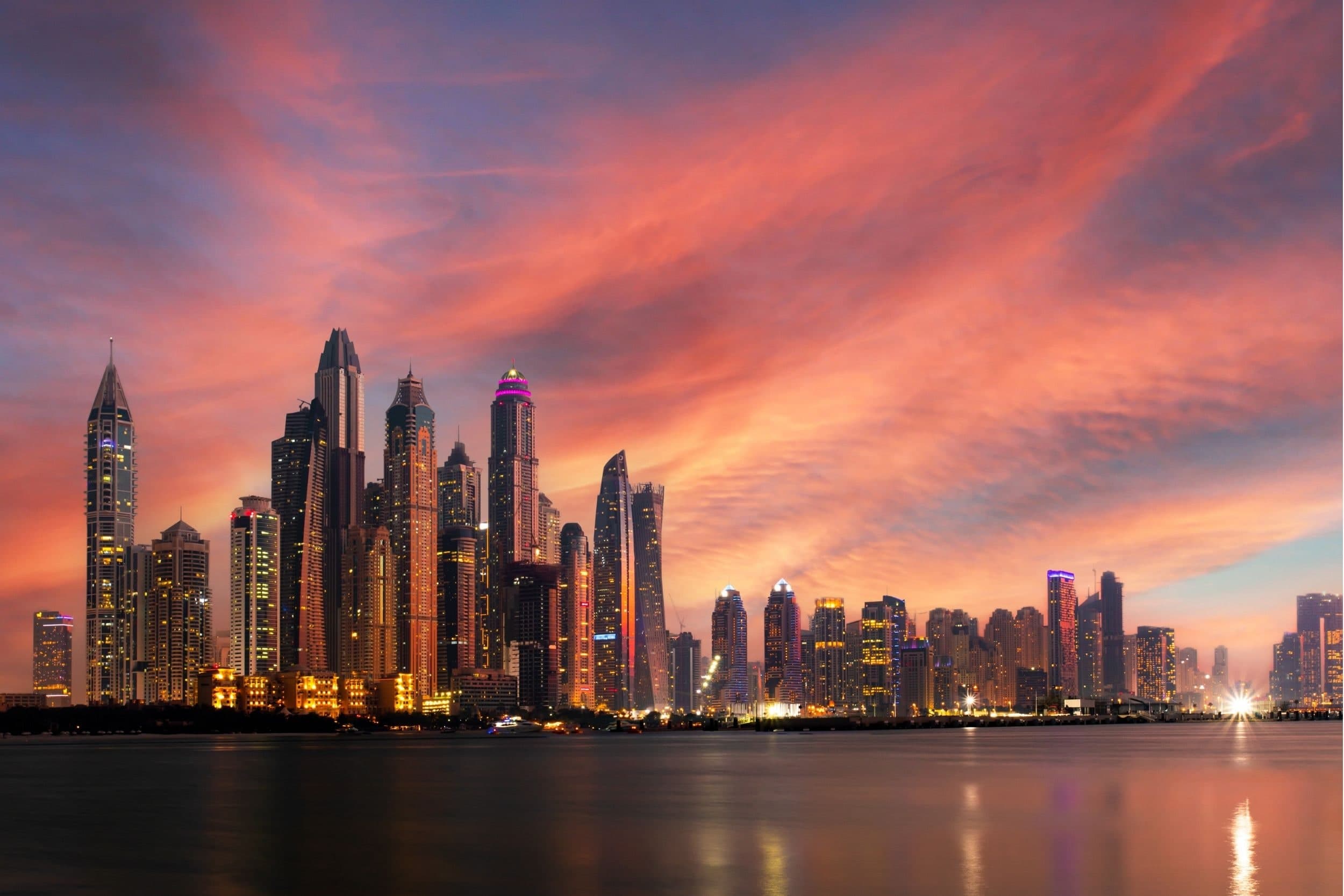 The towers of Dubai Marina silhouetted against a red and orange sunset sky, reflected in the water