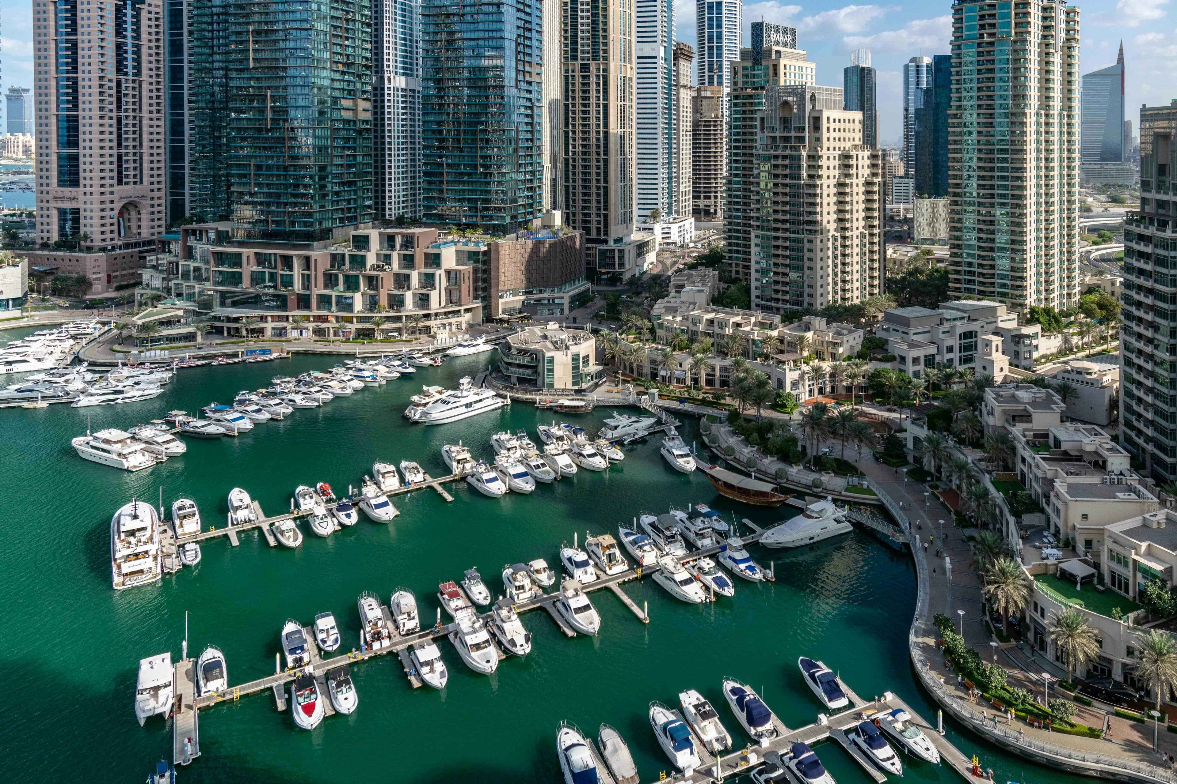 Yachts moored in rows at the Dubai Marina berths, with the promenade curving past and residential towers behind