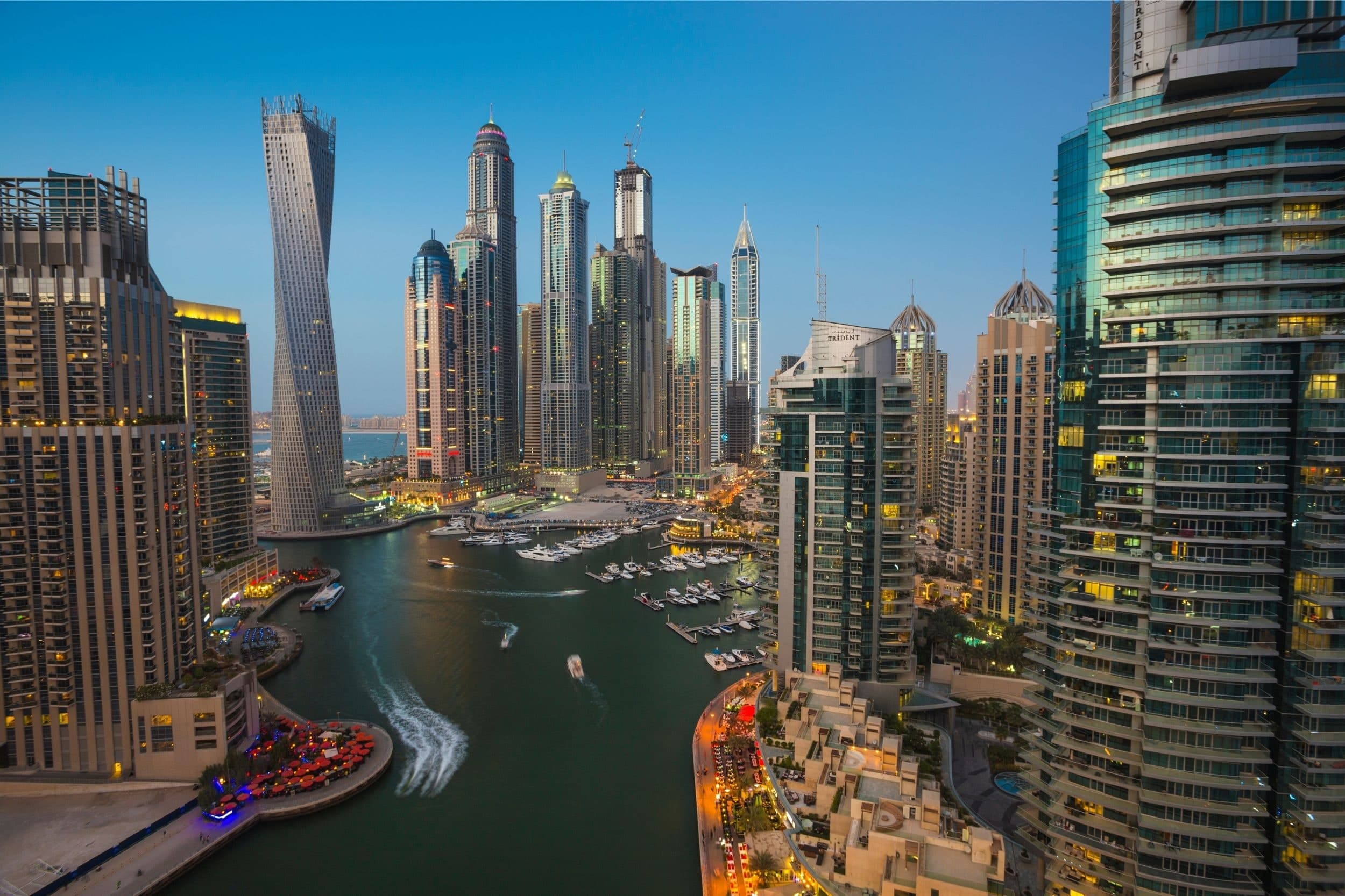 The Dubai Marina canal at dusk from high above, with the twisting Cayan Tower and boats on the water between the towers